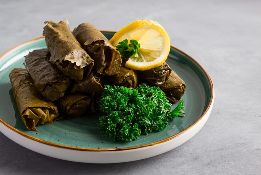 Dolma, cabbage rolls, grape leaves with filling, white sauce, lemon and herbs, rustic,