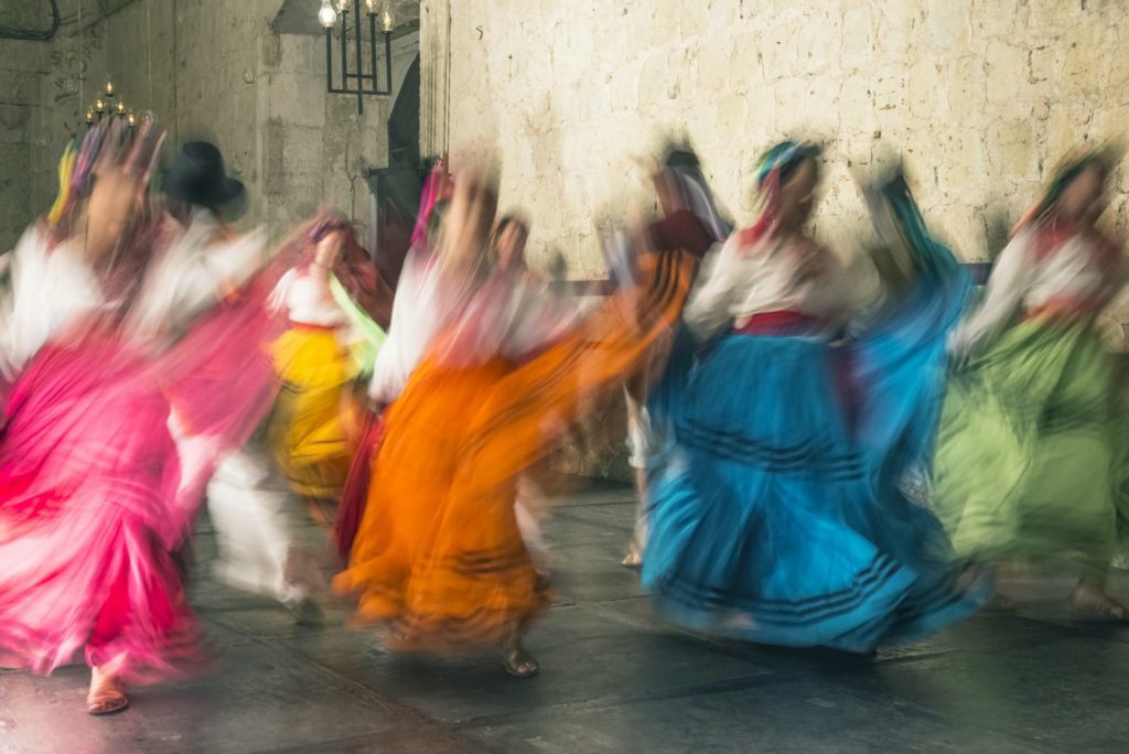 Blurred view of women dancing in traditional costumes, with bright coloured skirts